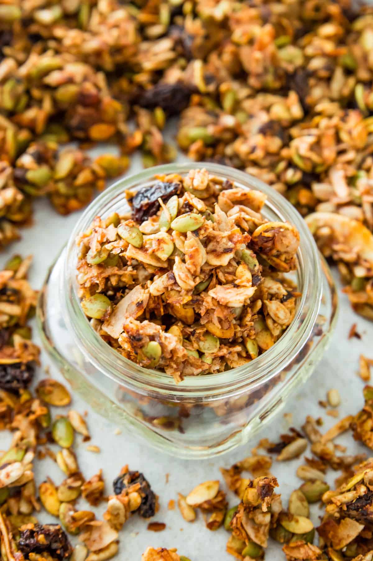 A jar filled with grain free granola sitting on a baking sheet with granola on it.