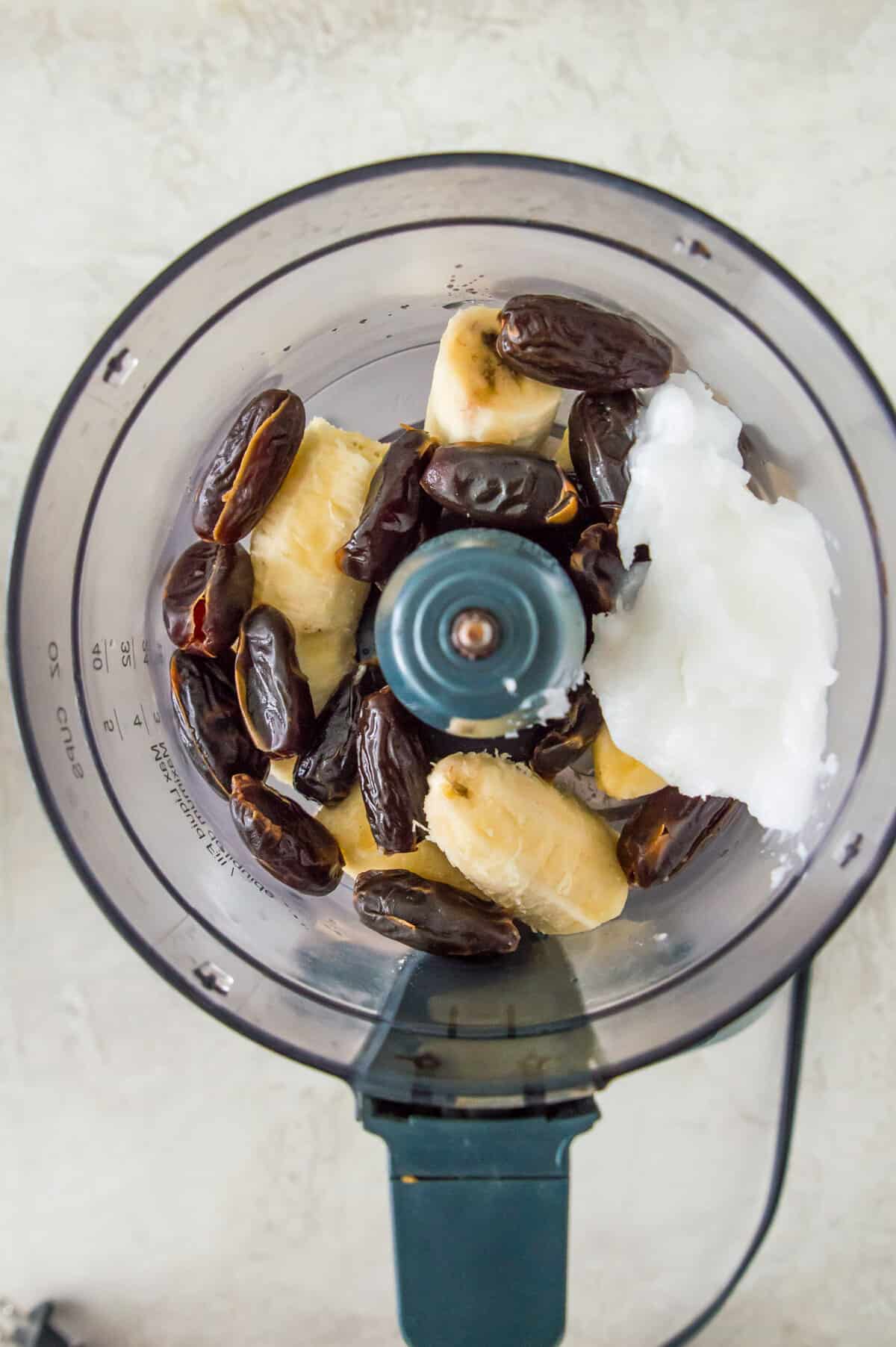 A food processor with dates, banana, coconut oil and vanilla extract in it.