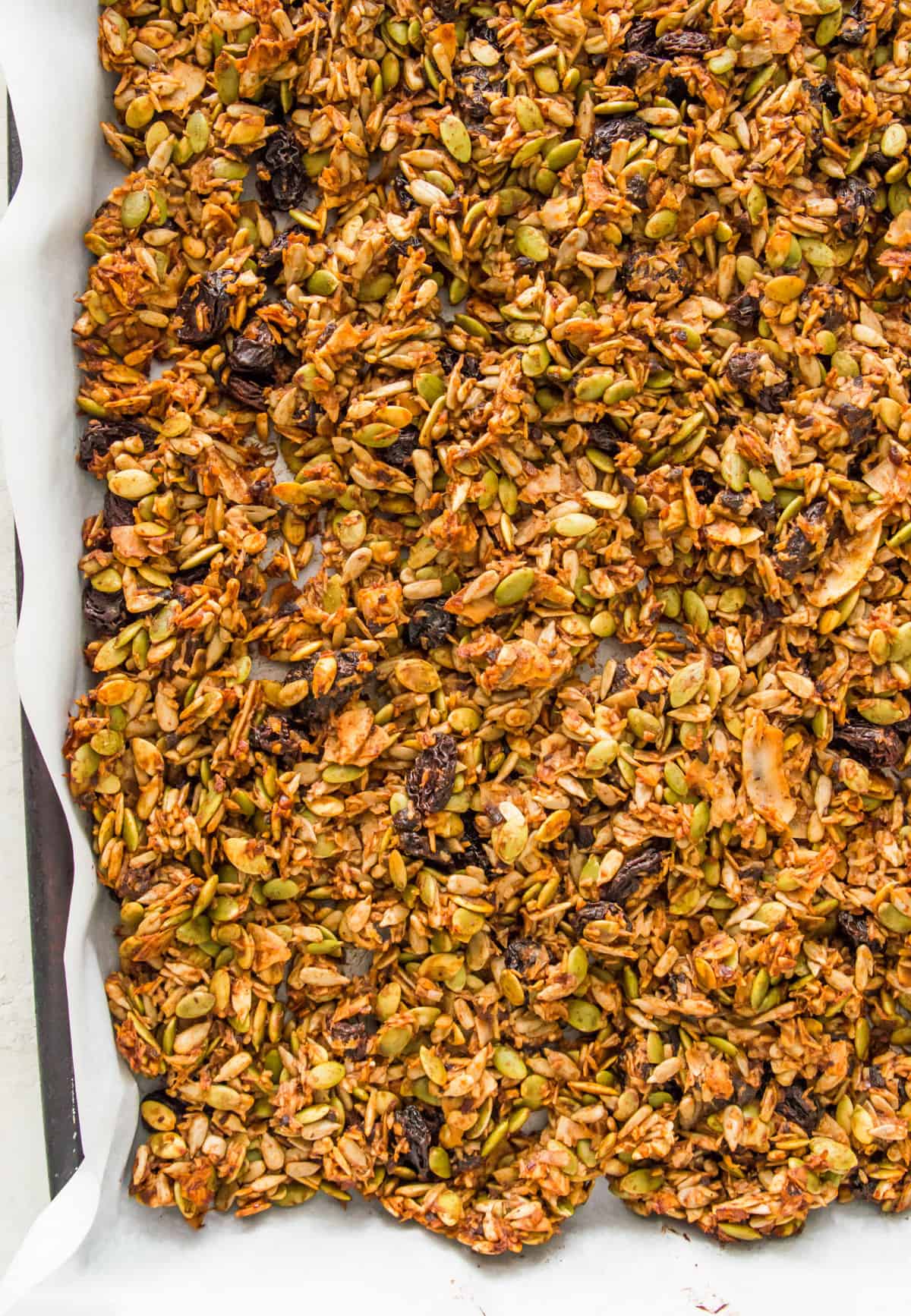A baking sheet lined with parchment paper with cooked granola on it.
