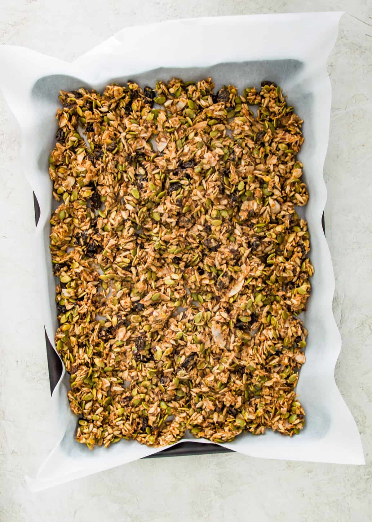 A baking sheet lined with parchment paper with granola spread out on it.