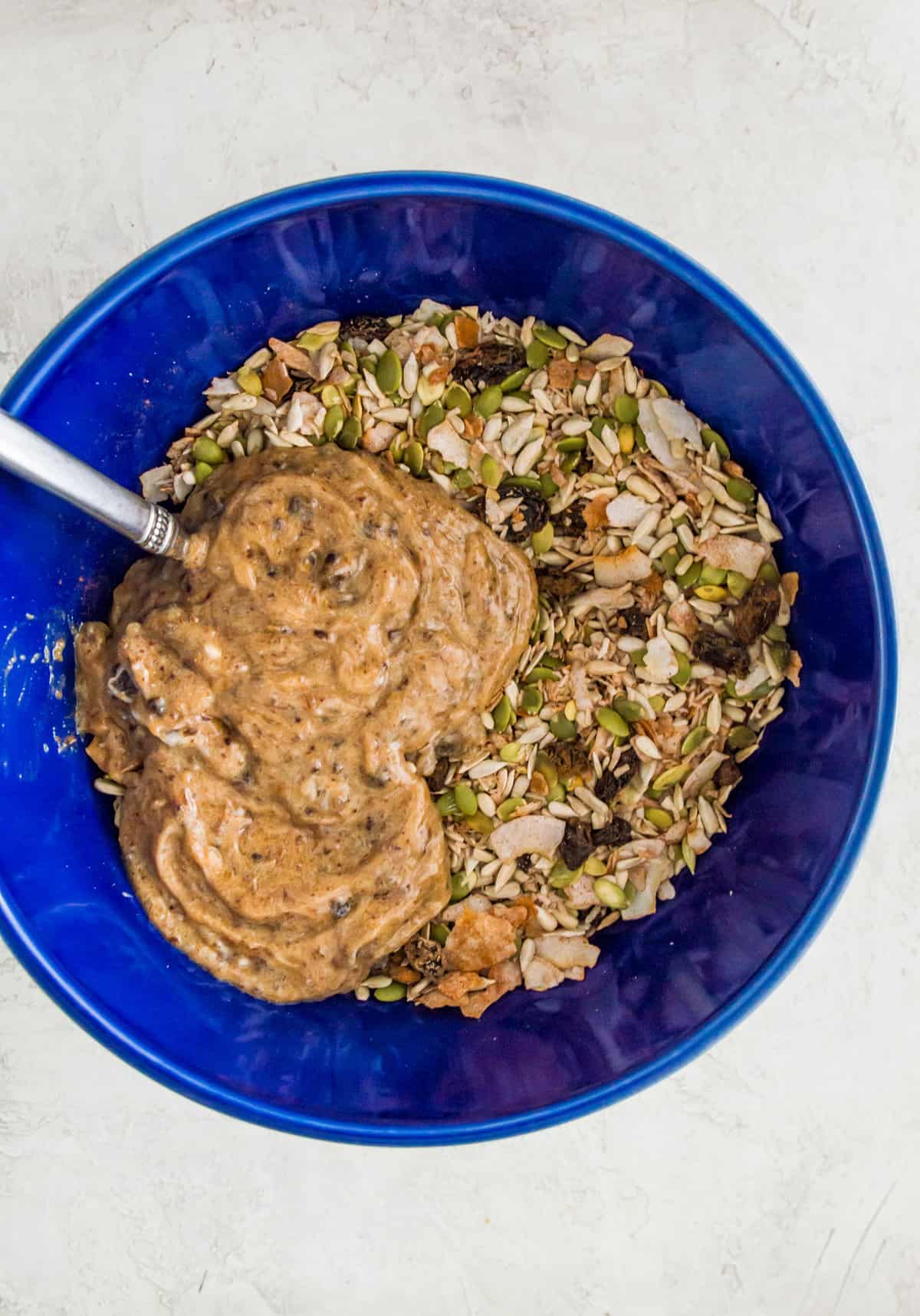 A large blue bowl with mixed nuts and seeds in it topped with a banana date paste. 