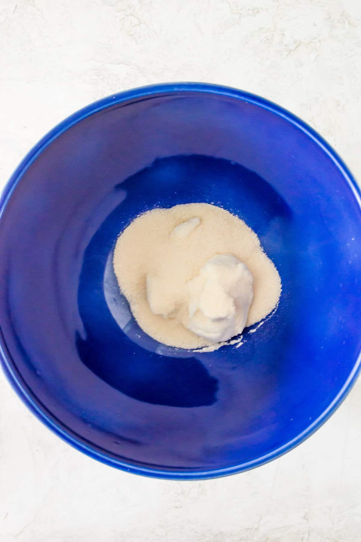 Cream cheese and cane sugar in a large blue bowl.