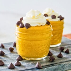 Two clear jars filled with pumpkin mousse topped with whipped cream and chocolate chips.