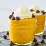 Two clear jars filled with pumpkin mousse and topped with whipped cream and chocolate chips.