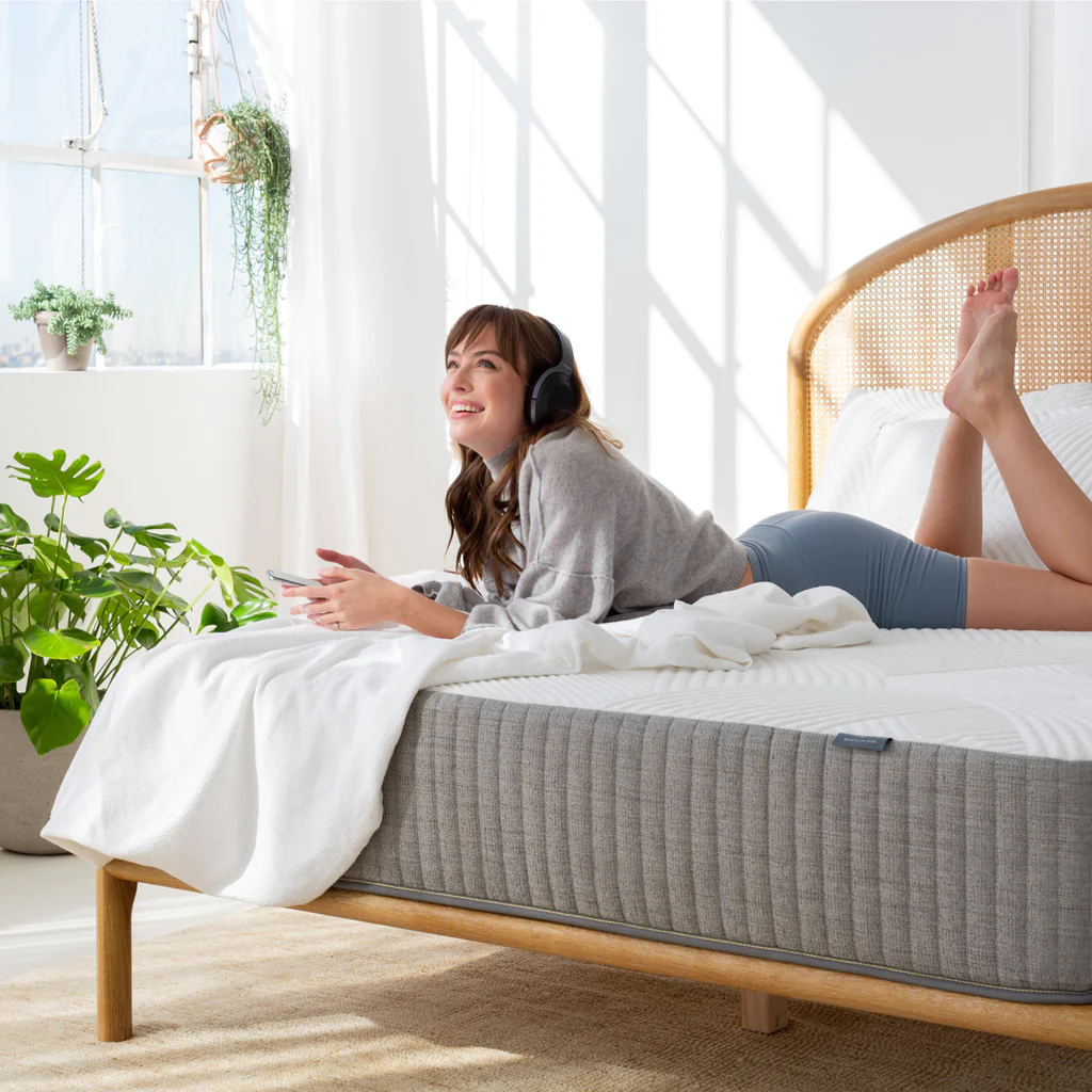 A woman laying on a Brentwood Home mattress with headphones on and a blanket under her. 