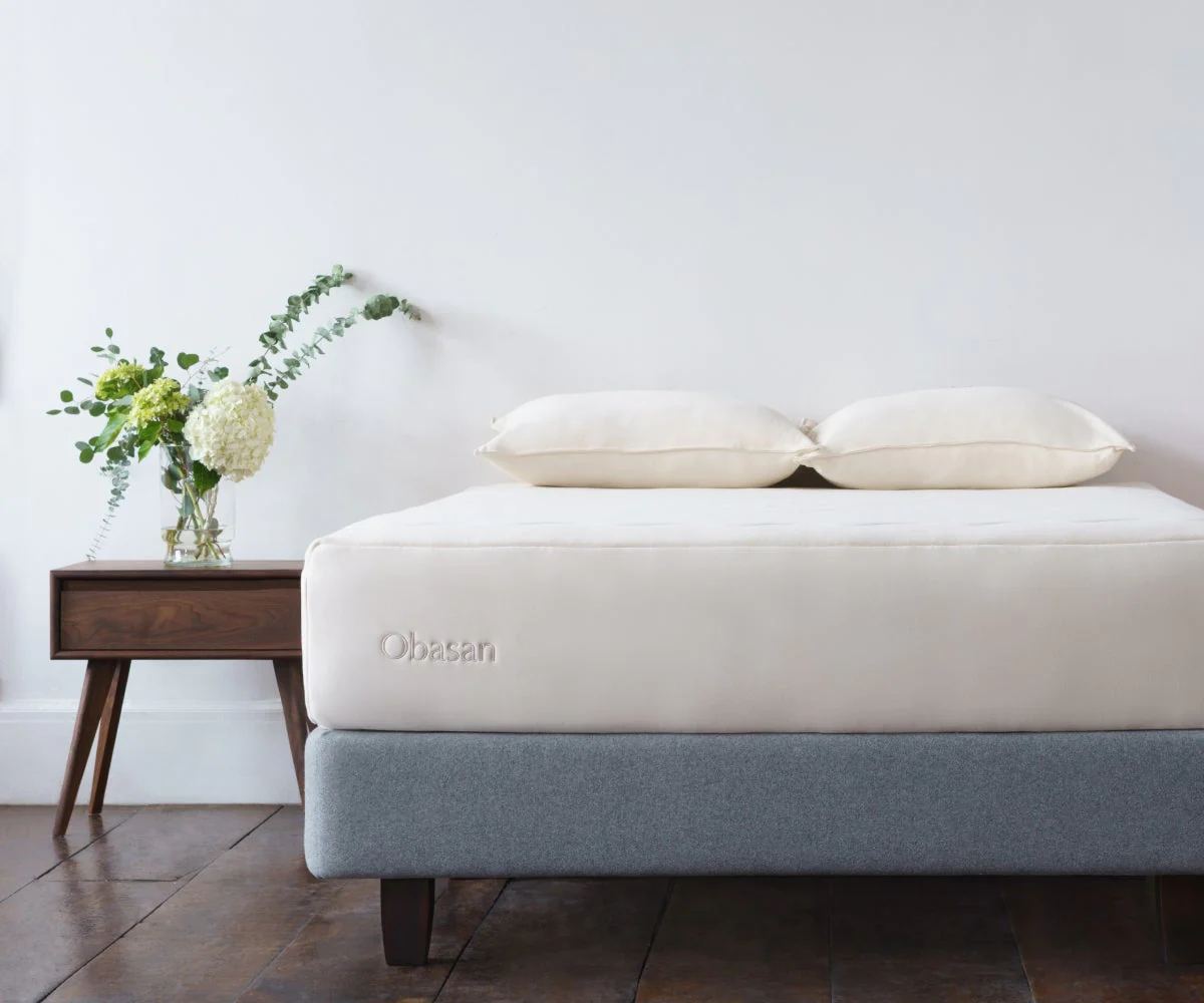 An Obasan mattress on a bed frame with a wooden side table beside it that has white flowers in a vase.