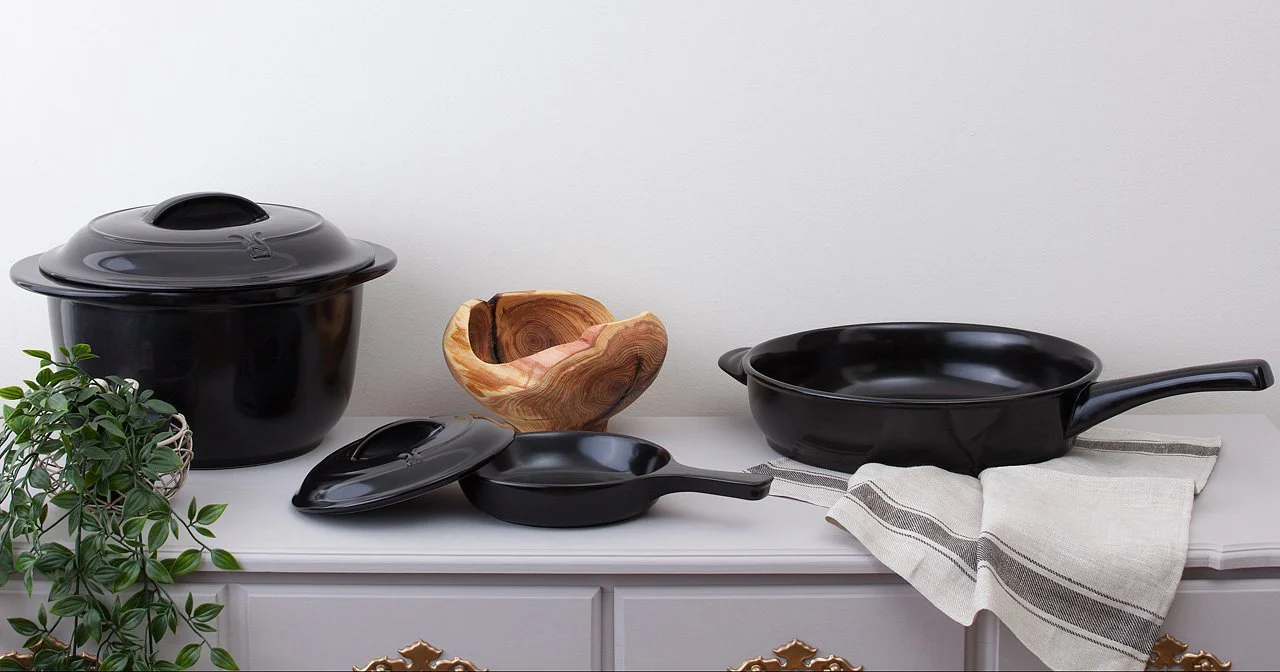 A white counter top with black ceramic pots, pans and dutch ovens from Xtrema cookware on it.