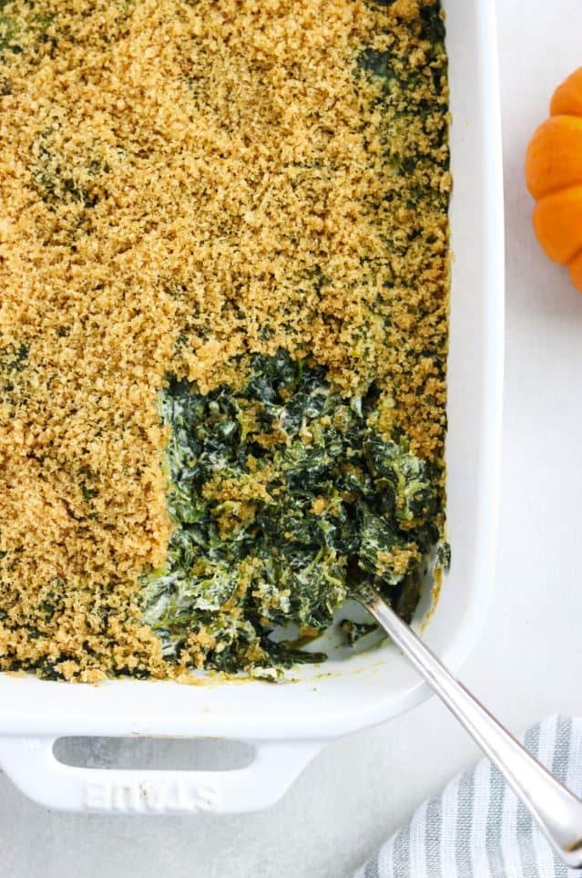 A baking dish with paleo creamy spinach casserole and a serving spoon.