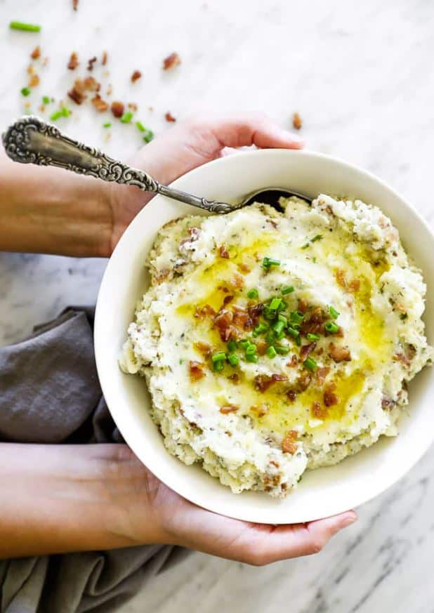 A person holding a bowl full of paleo loaded mashed cauliflower over a kitchen towel and granite counter.