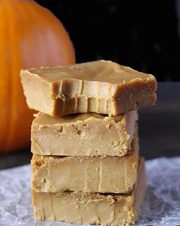 Four pumpkin fudge squares stacked on top of parchment paper and the top square has a bite out of it.