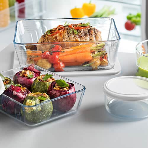 Glass bakeware with roasted vegetables and a cooked ham in them. 