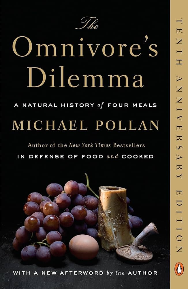 The cover of the book The Omnivore's Dilemma which has a black background, white text and food on it including purple grapes, an egg and mushroom. 