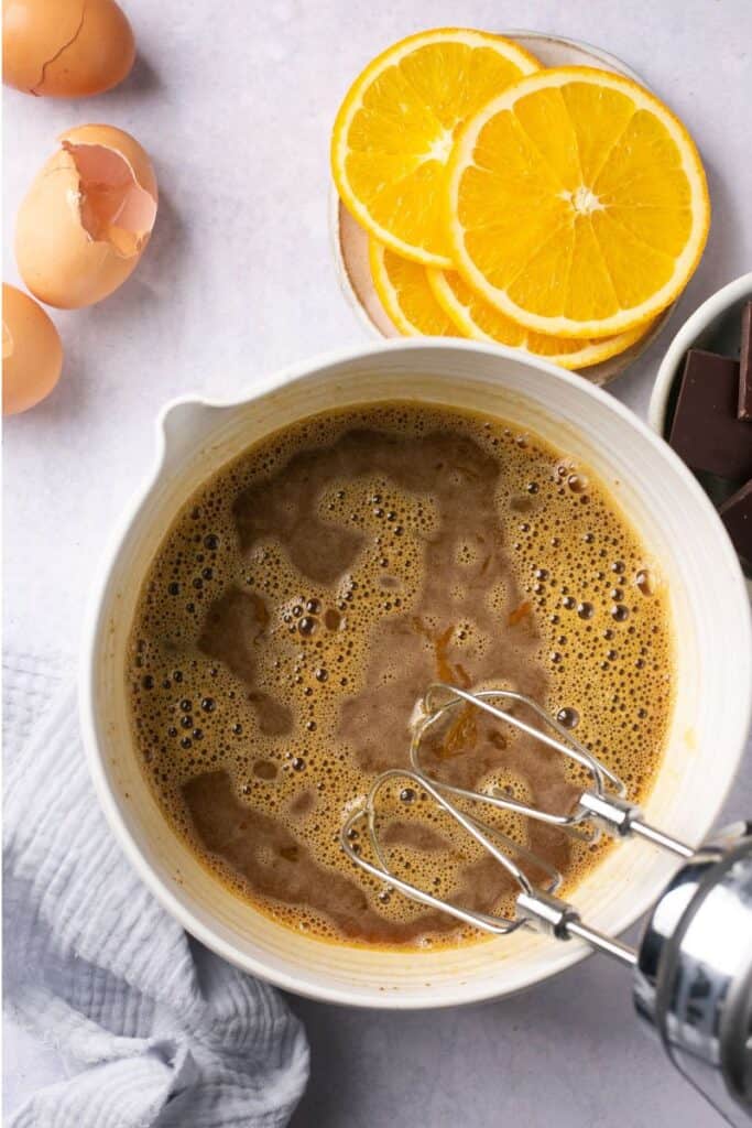 A bowl with eggs and sugar in it that have been whipped with a hand blender.