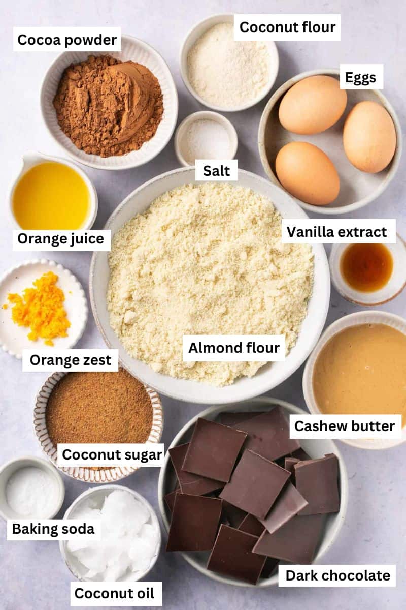 The ingredients needed to make chocolate orange brownies in separate bowls including almond flour, orange juice, eggs, orange zest, coconut sugar and cocoa powder.