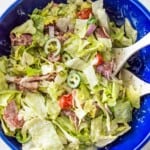 An Italian grinder salad in a large blue bowl topped with cherry tomatoes, chopped banana peppers and parmesan cheese.