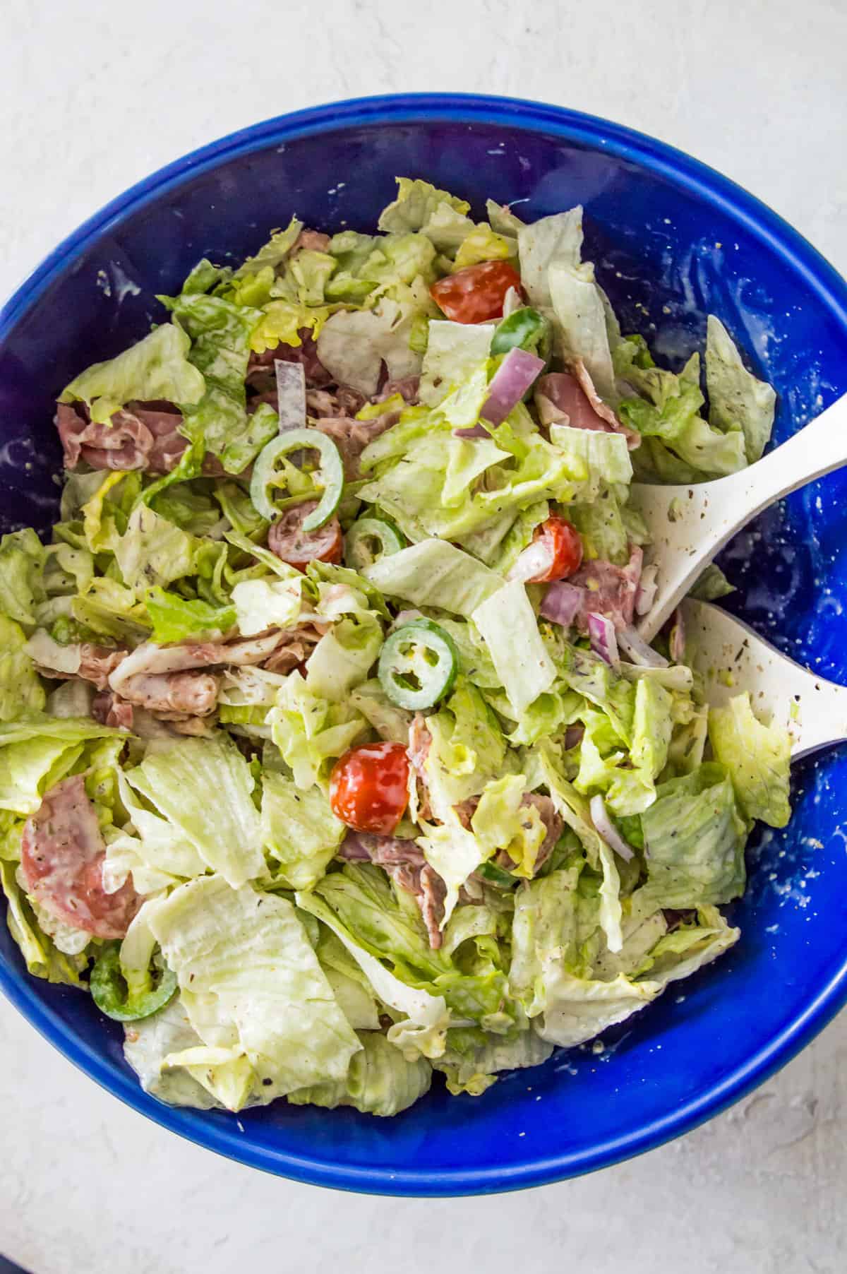 A large blue bowl with a salad in it made with chopped lettuce, baby tomatoes, salami and chopped banana peppers. 
