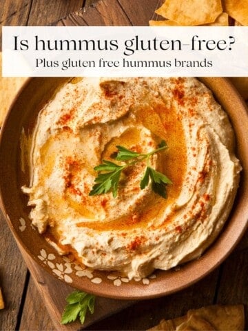 A bowl of hummus garnished with fresh parsley with pita chips around it.