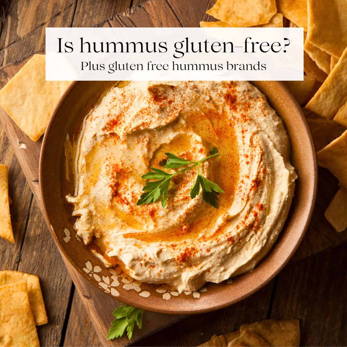 A bowl of hummus garnished with fresh parsley with pita chips around it.