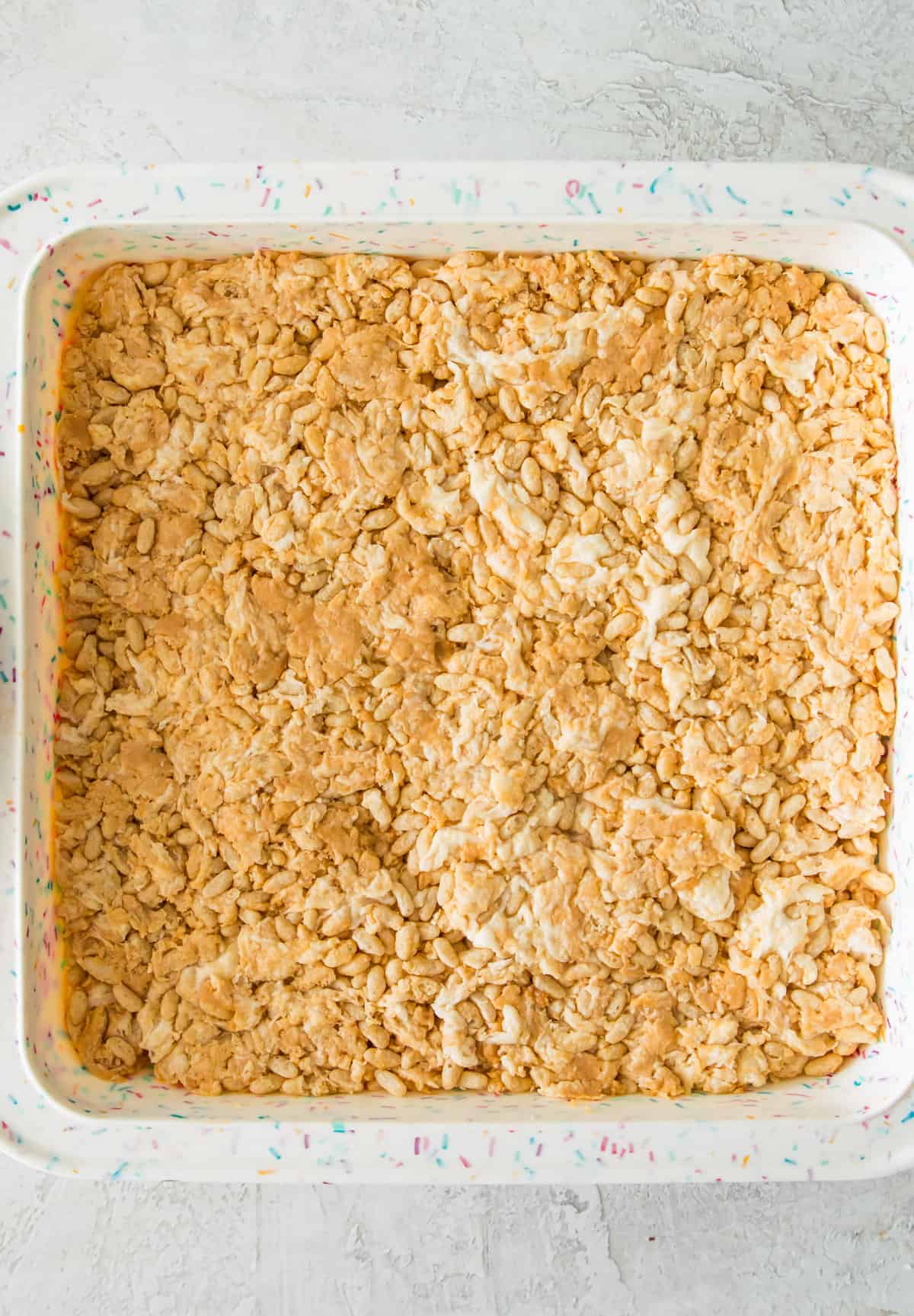 A mixture of Rice Krispie cereal, melted marshmallows and peanut butter in an even layer in a square baking pan.