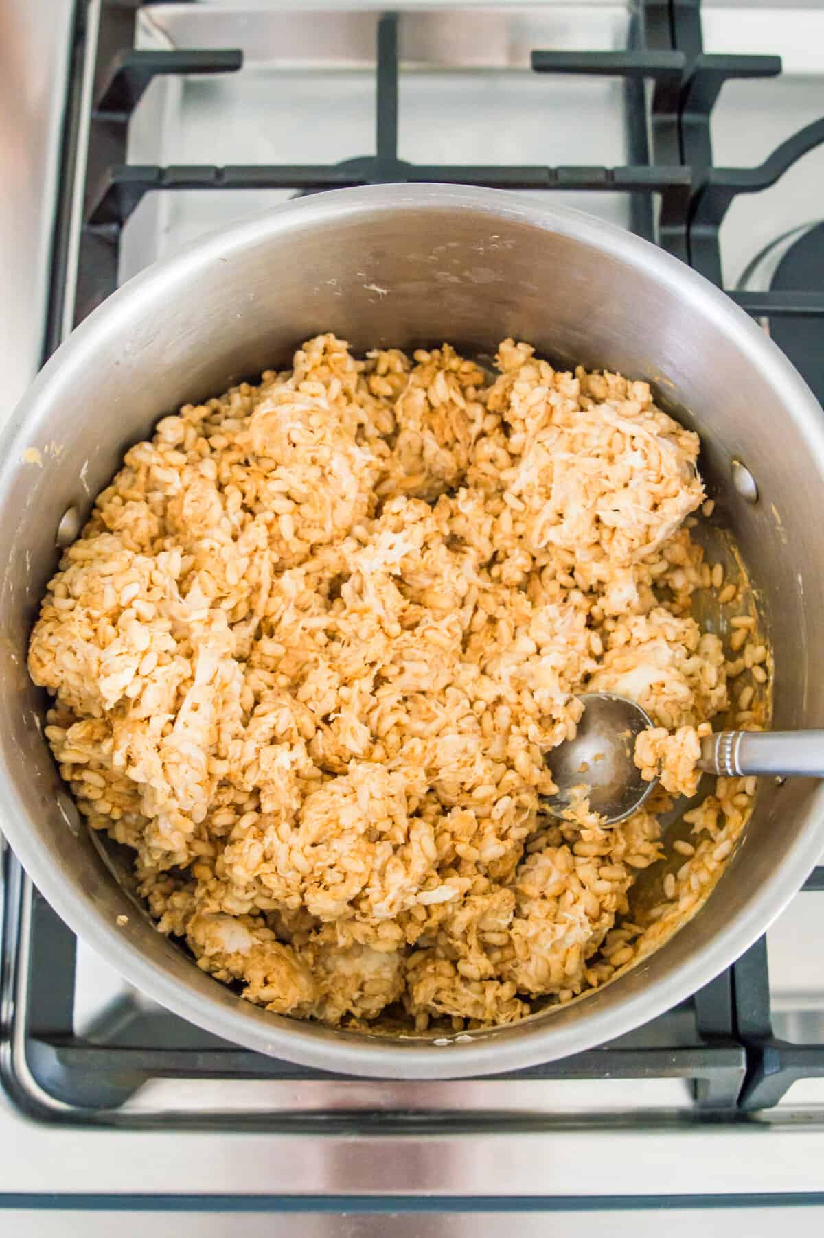A large pot on the stovetop with rice crispy cereal in it coated in a melted marshmallow and peanut butter mixture.
