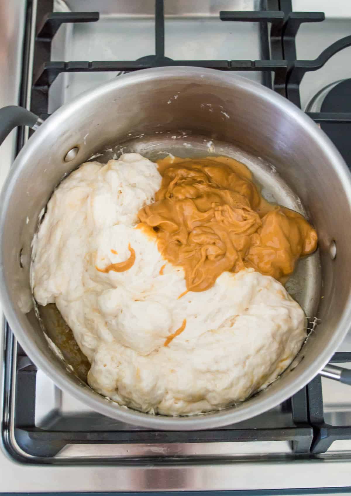 A large pot on the stovetop with melted marshmallows and smooth peanut butter in it.