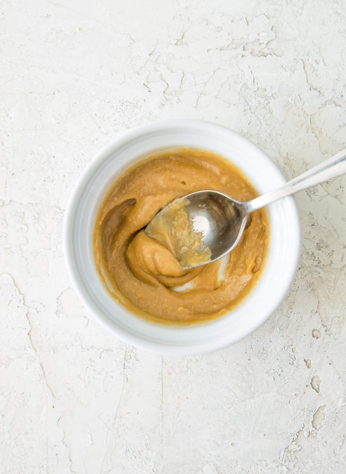 A caramel sauce in a bowl with a spoon in it.