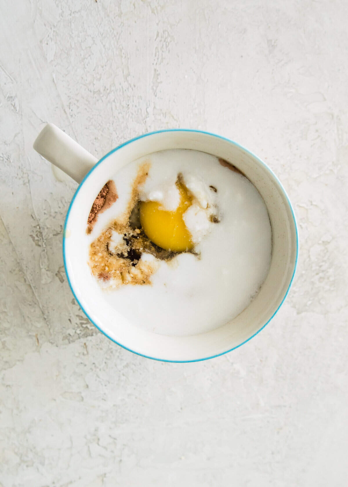 A mug with an egg, flour, cocoa powder and coconut milk in it.