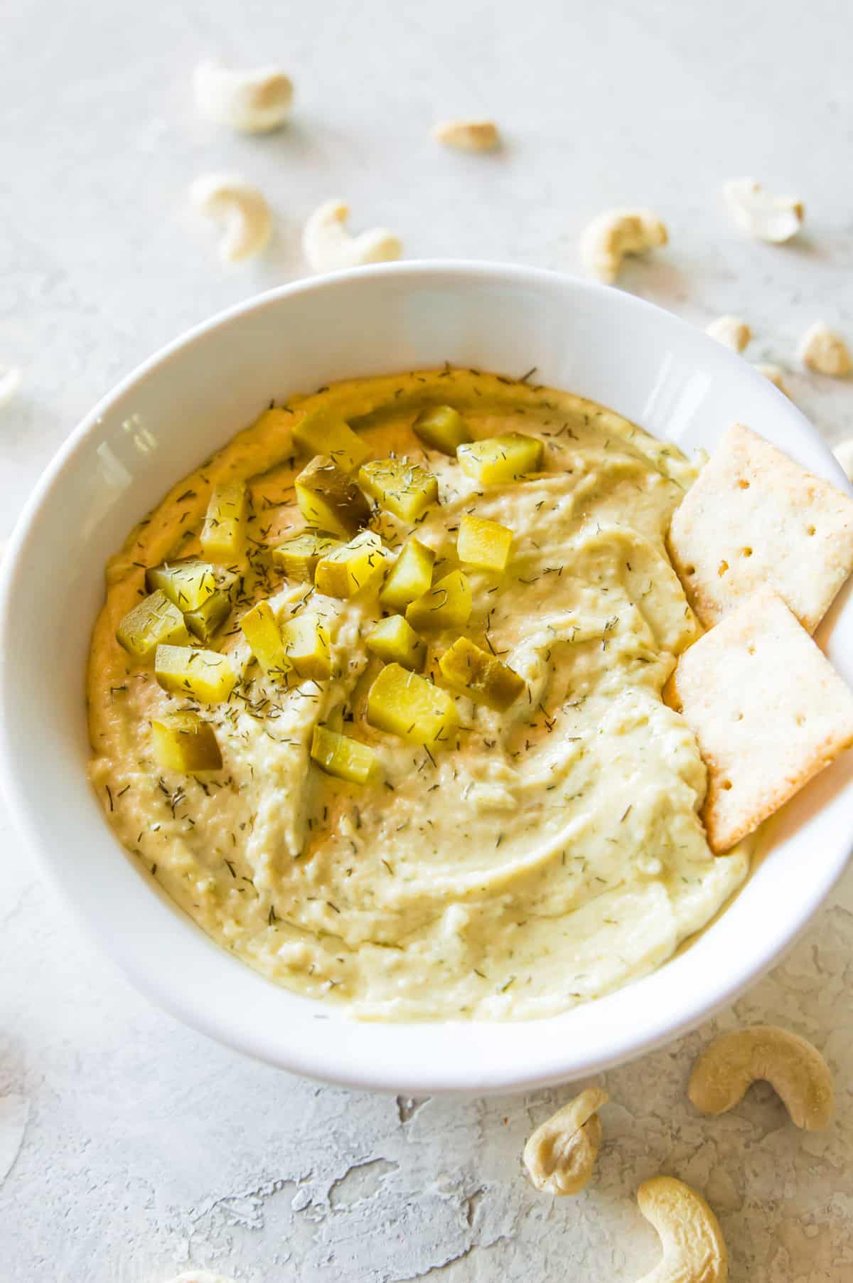 A bowl of dill pickle dip topped with chopped dill pickles, fresh dill and with two crackers in it.
