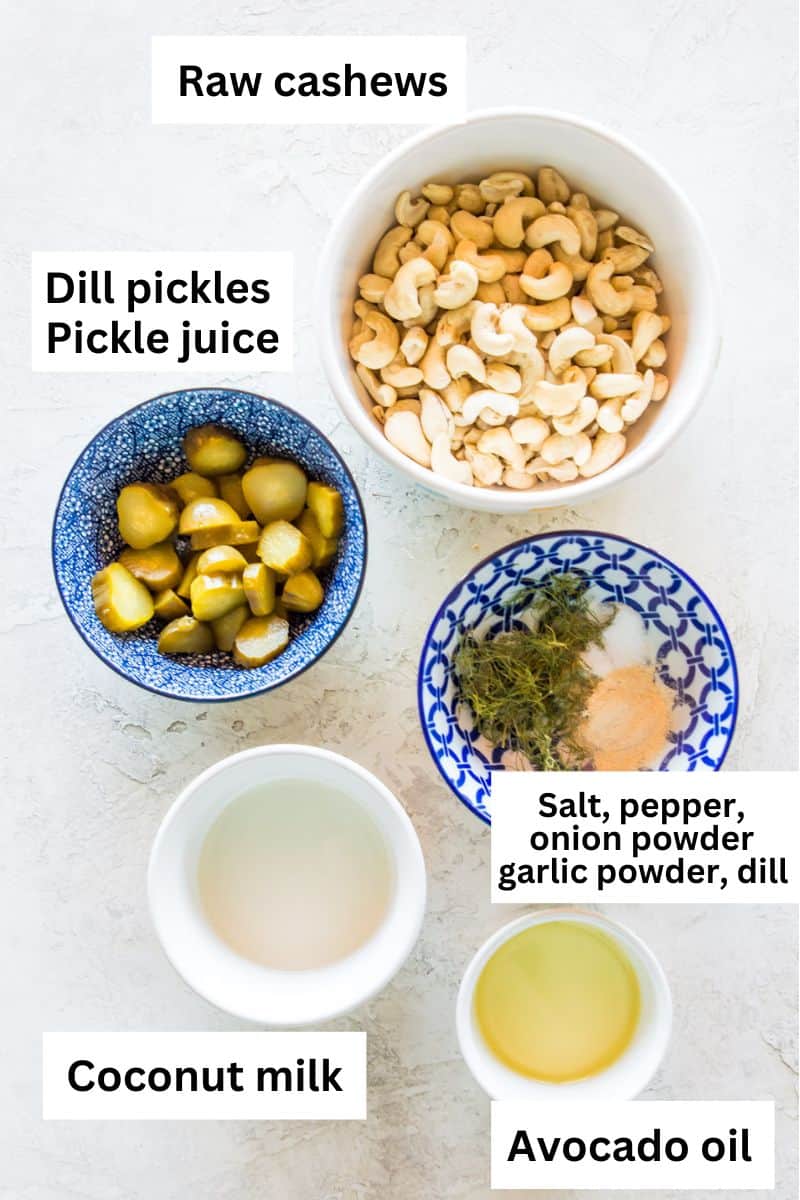 The ingredients needed to make a dill pickle dip separated into bowls including chopped dill pickles, raw cashews, avocado oil and spices.