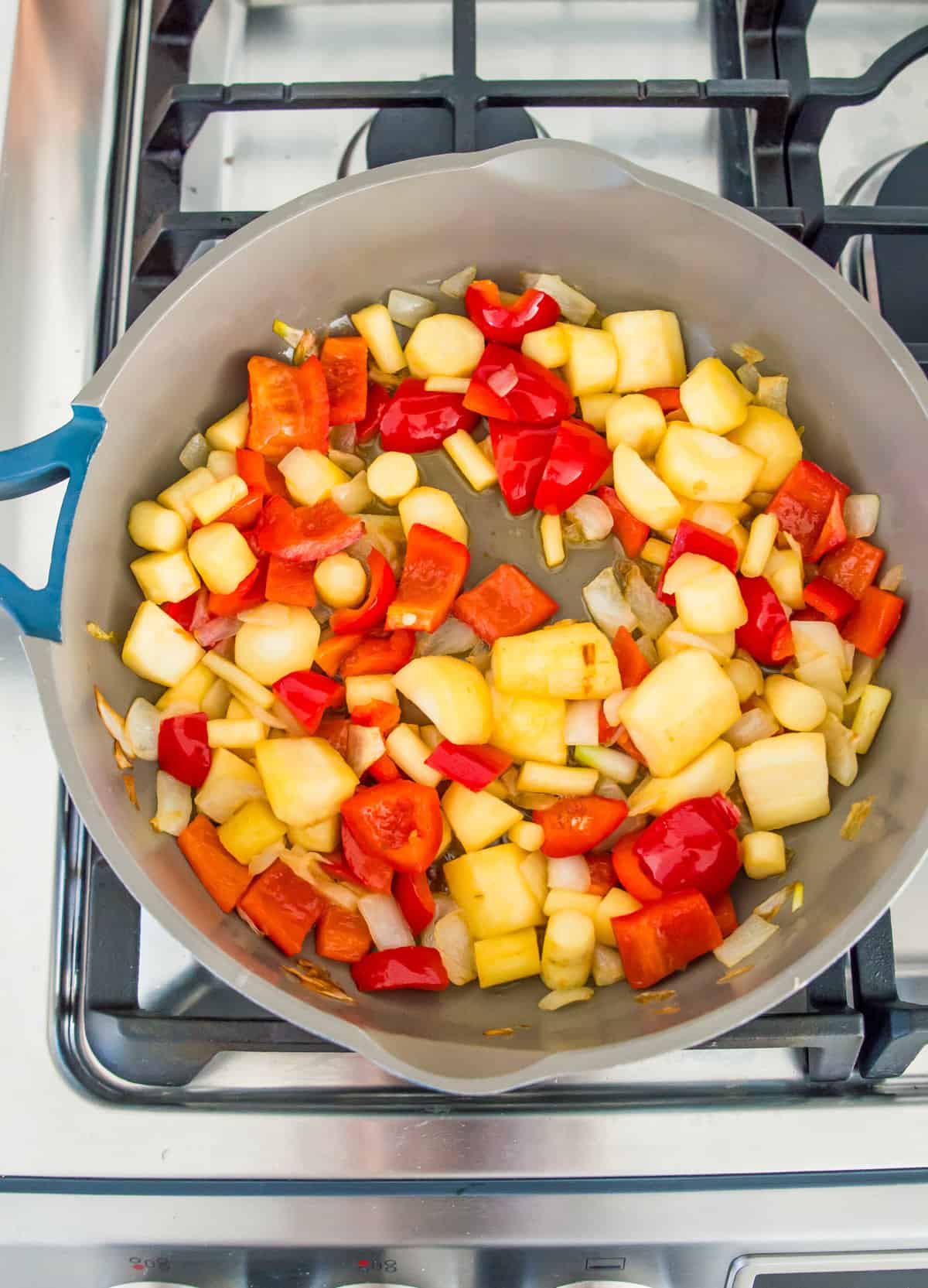 A grey pan on the stovetop with cooked chopped red bell peppers, parsnips and onions in it.