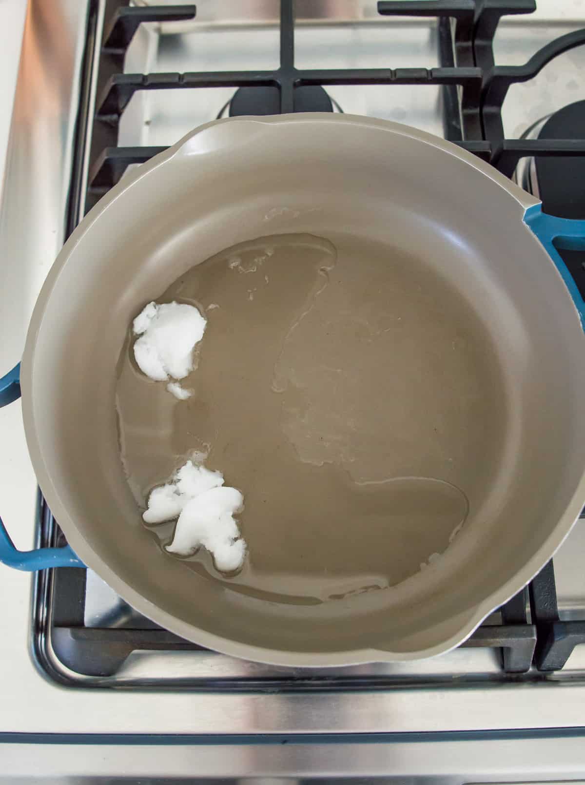 A blue frying pan on the stovetop with coconut oil in it.