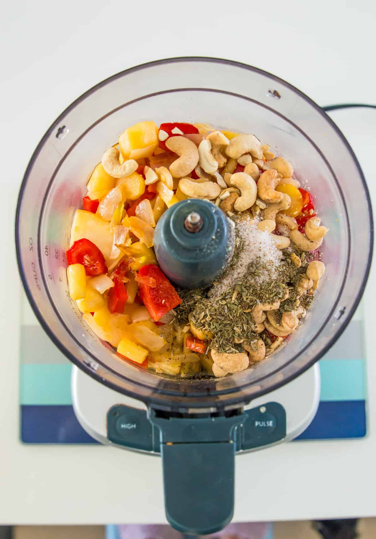 A food processor with cashews, chopped parsnips, chopped red bell pepper and spices in it.