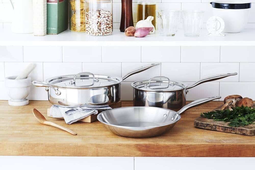 A set of stainless steel pots and pans from Heritage Steel sitting on a wooden countertop.