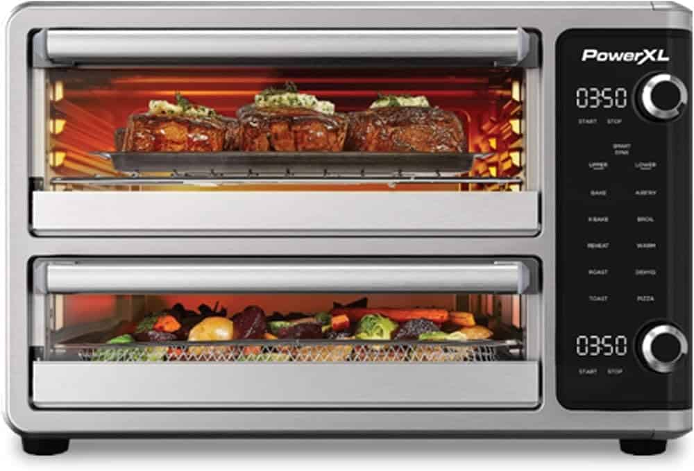 A toaster oven with two sections with steak and vegetables cooking in it.