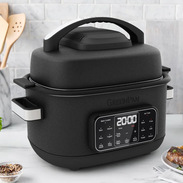 A GreenPan black air fryer sitting on a countertop with a plate of food beside it.