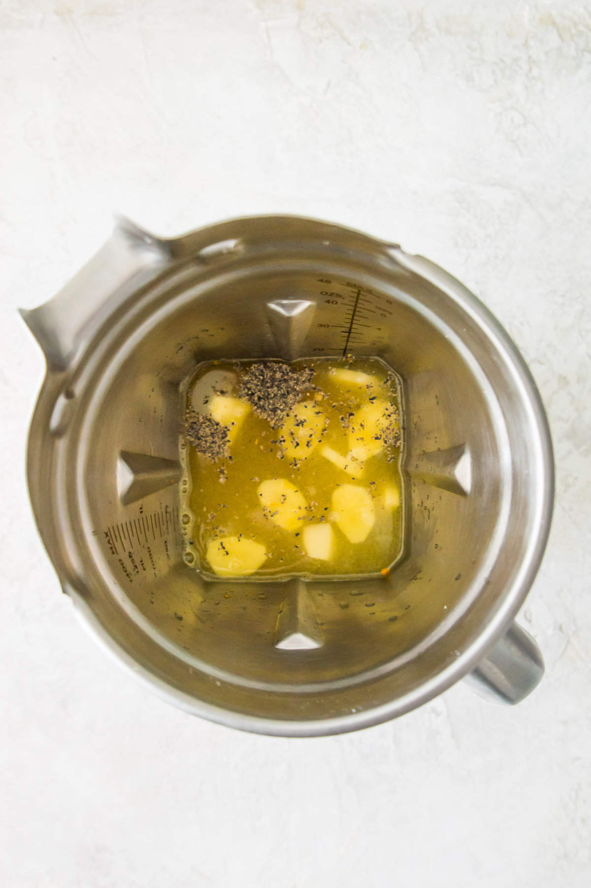 A blender filled with water, pieces of ginger, turmeric and black pepper.