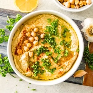 A bowl of gluten free hummus topped with chopped fresh parsley and chickpeas.