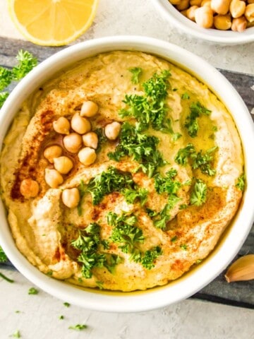 A bowl of gluten free hummus topped with chopped fresh parsley and chickpeas.