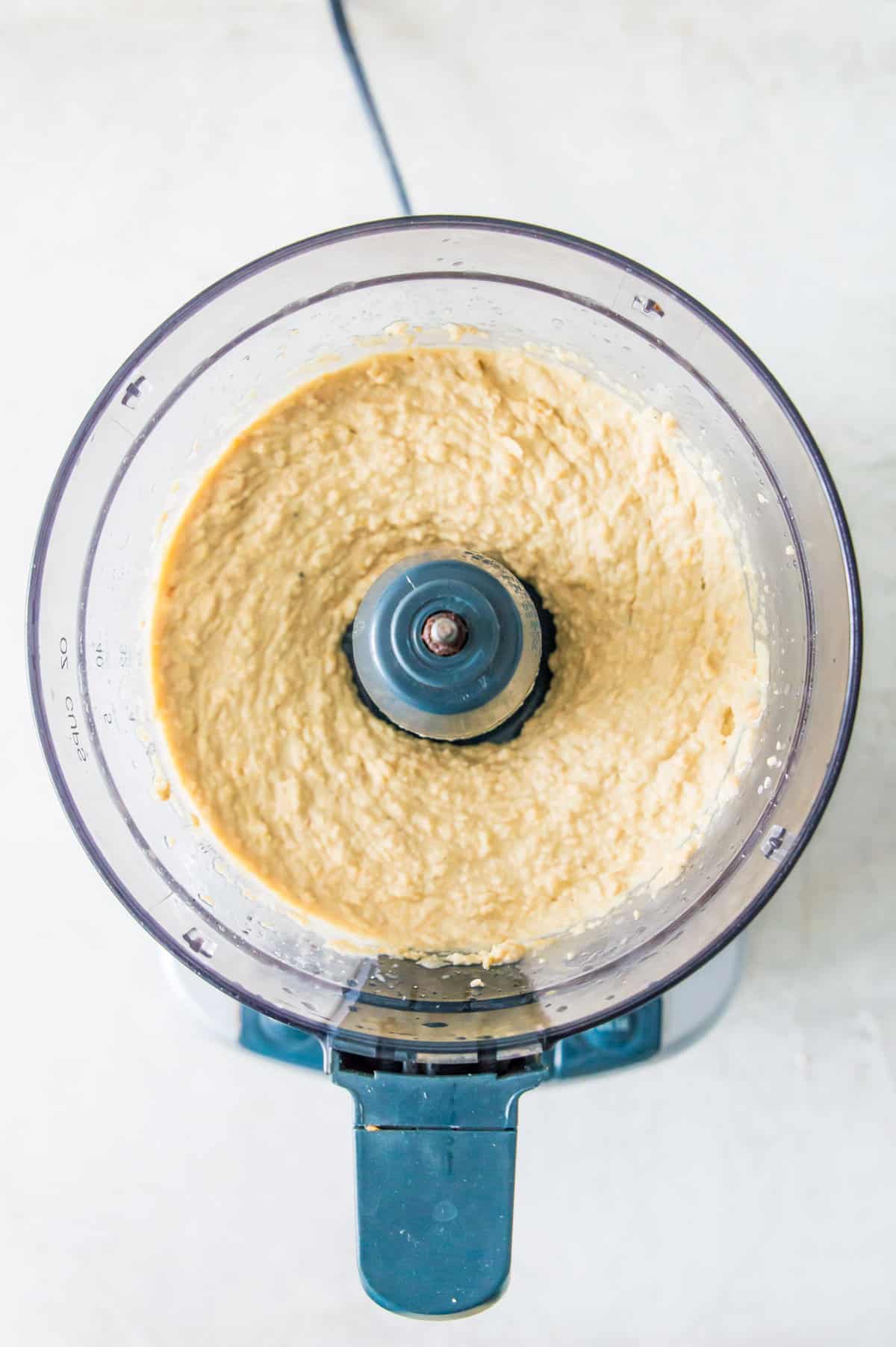 A food processor filled with a blended hummus dip.