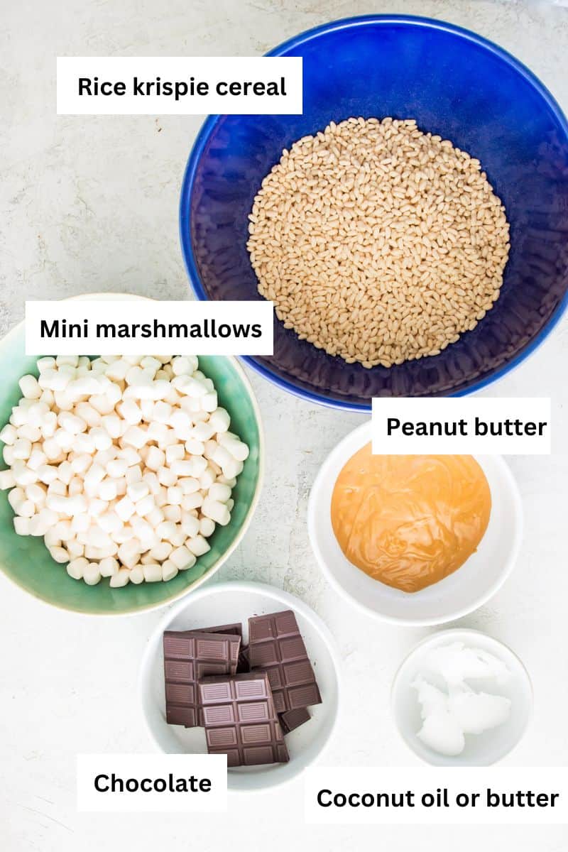 The ingredients needed to make chocolate peanut butter Rice Krispie treats separated into bowls including rice krispie cereal, marshmallows, dark chocolate and peanut butter.