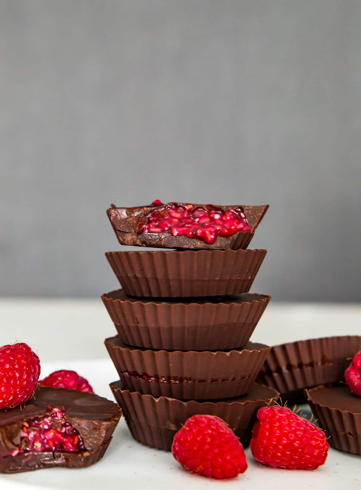 A stack of five chocolates and the top one has a bite out of it with a raspberry filling spilling out.