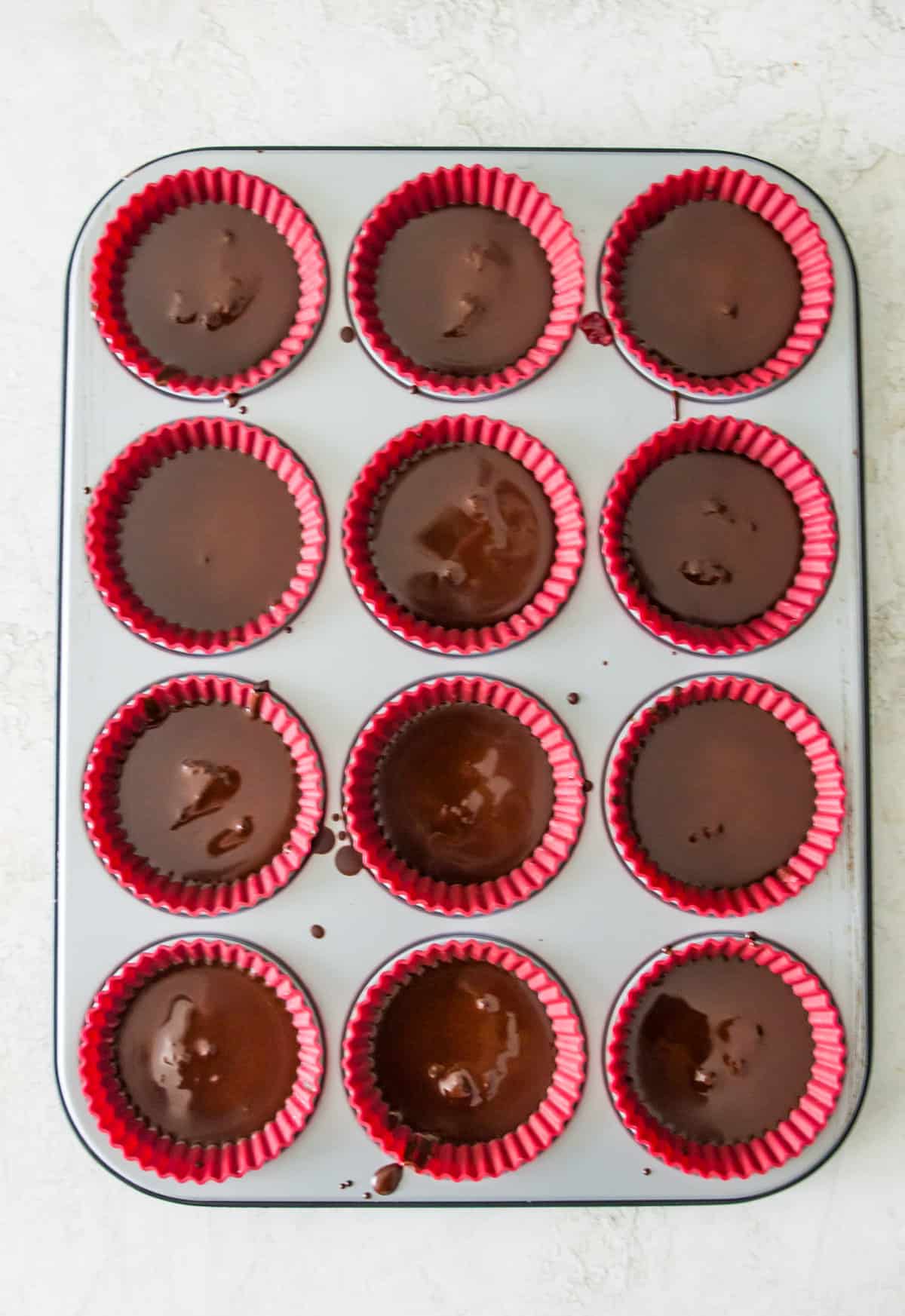 A muffin tray lined with silicone muffin cups and each one has melted chocolate in it.
