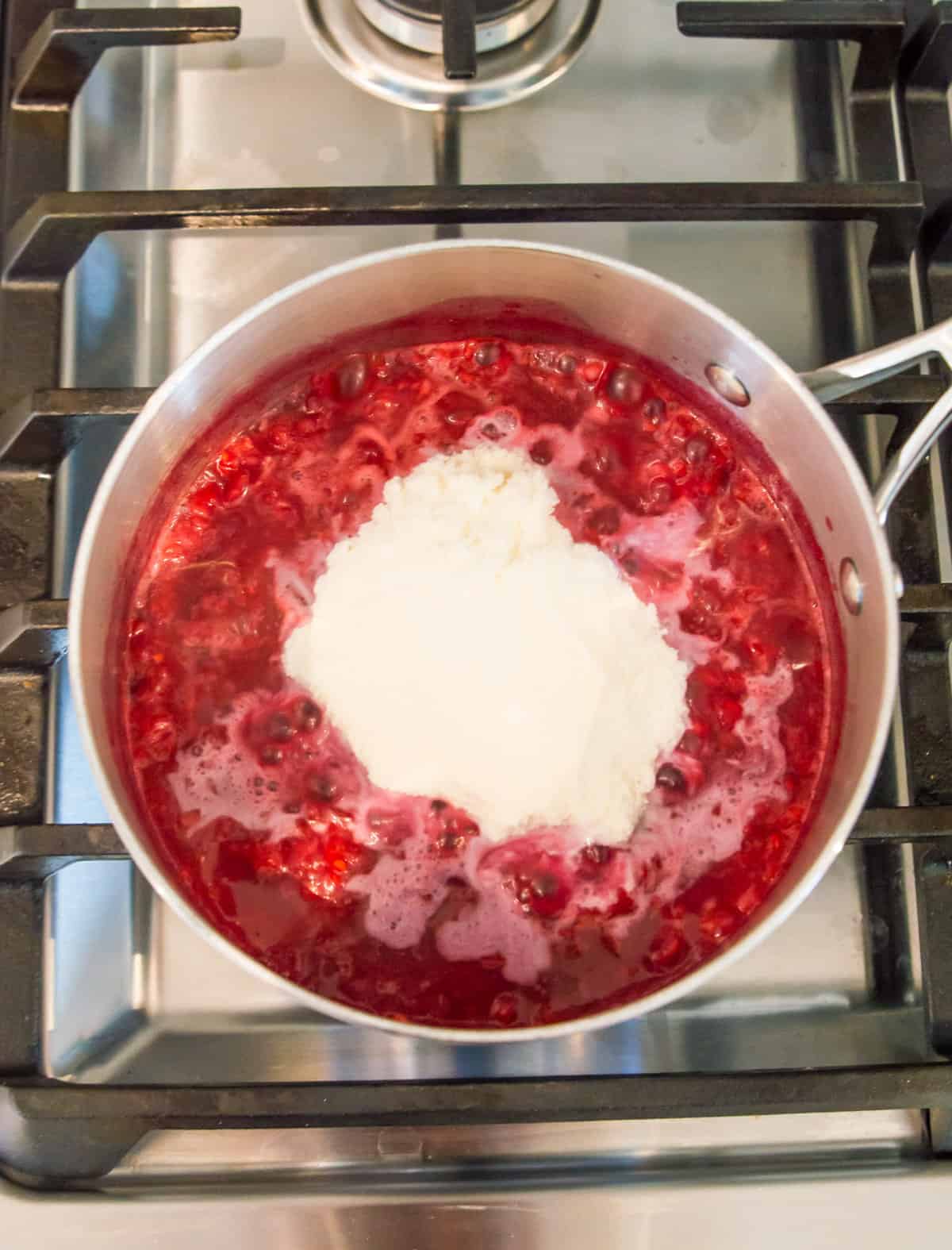 A pot of raspberries simmering on a stovetop with powdered collagen on top of them.