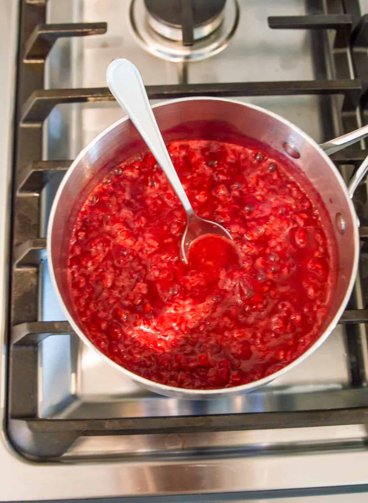 A pot of raspberries simmering on the stovetop with a spoon in it.