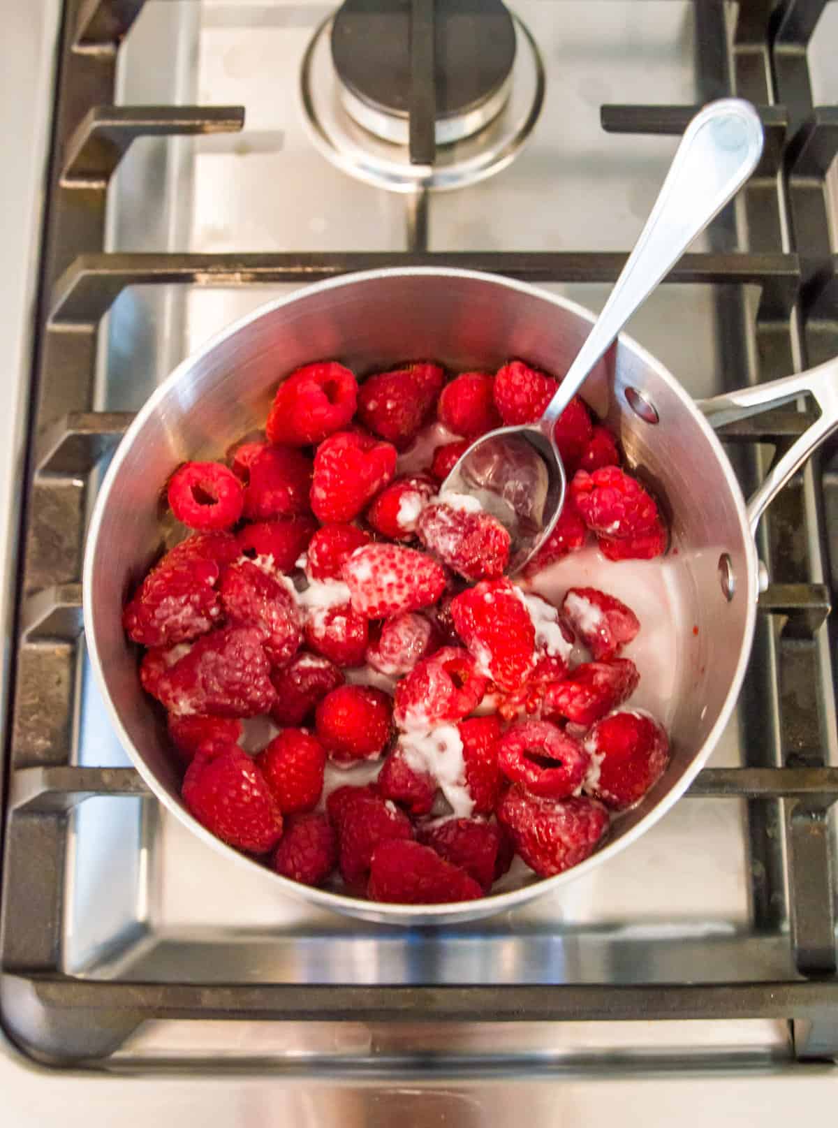 A pot with fresh raspberries, coconut milk and a spoon in it on the stovetop.