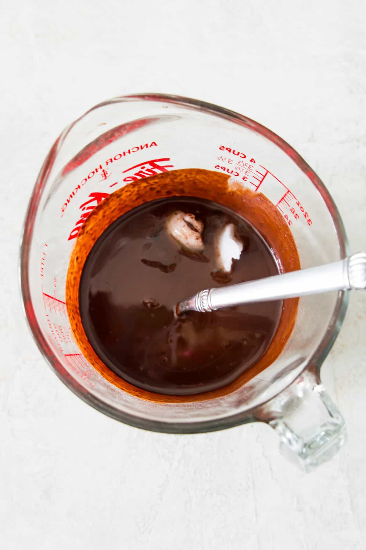 A glass measuring cup with melted chocolate and a couple clumps of coconut oil in it.