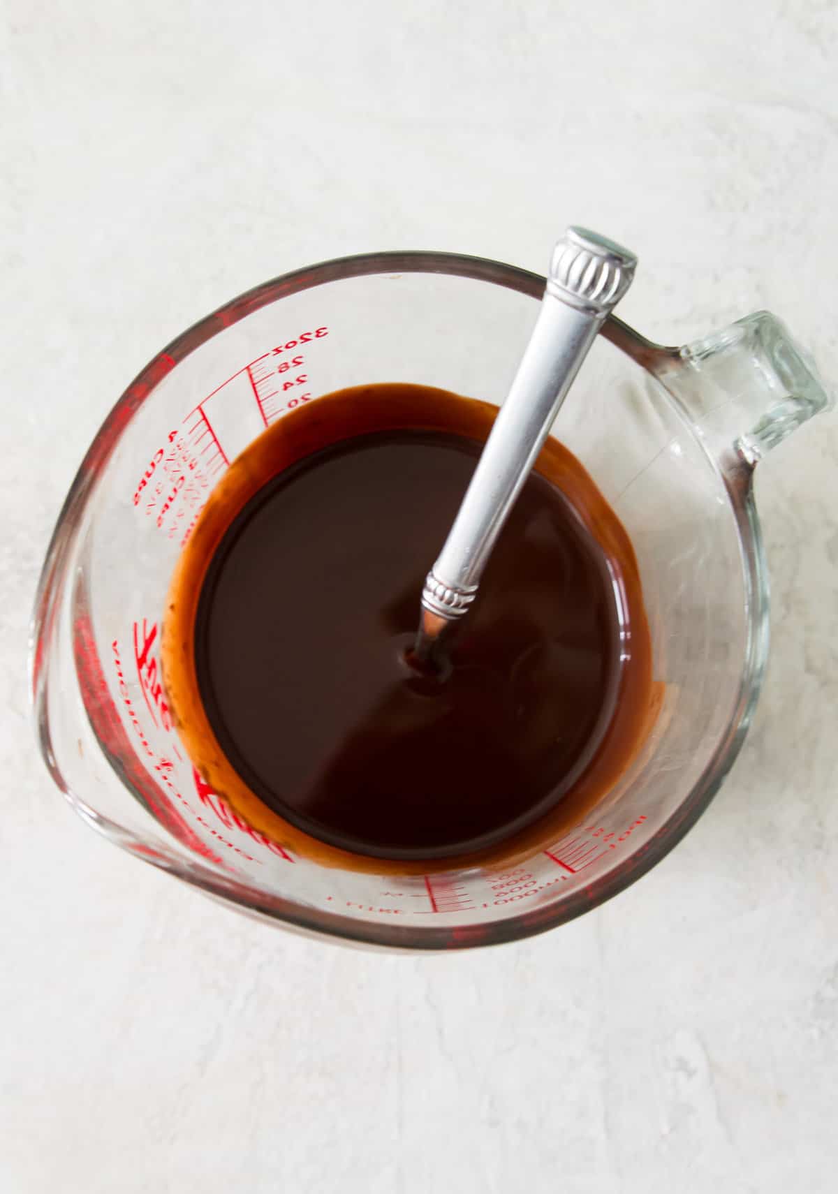 Melted chocolate in a large glass measuring cup with a spoon in it.