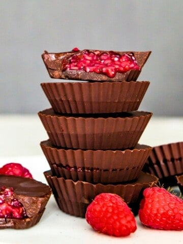 A stack of five chocolates and the top one has a bite out of it with raspberry filling spilling out of it.