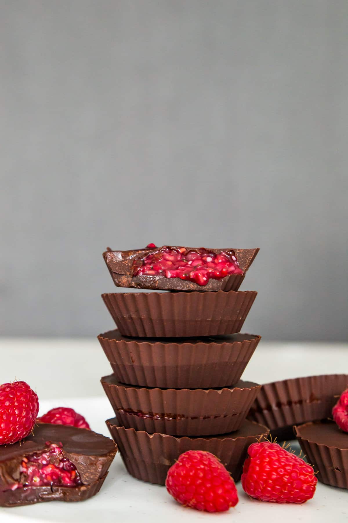 A stack of five raspberry filled chocolates and the top one has a bite out of it with the raspberry filling spilling out.