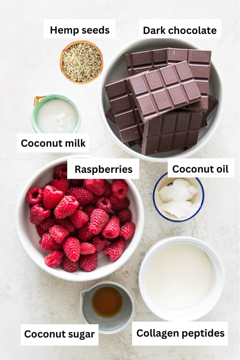 The ingredients needed to make raspberry filled chocolates separated into bowls including dark chocolate, fresh raspberries, coconut sugar, and coconut milk.